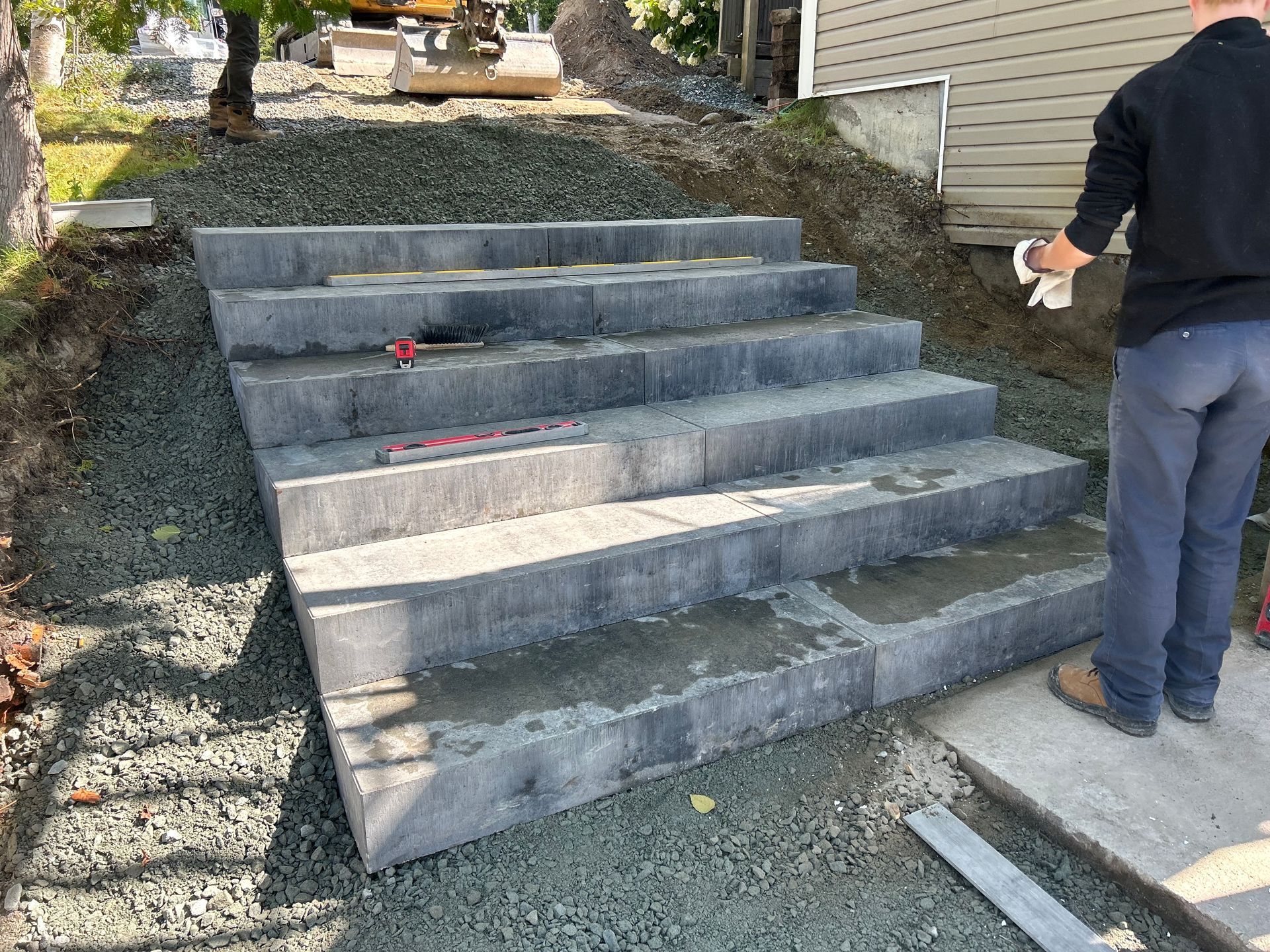 Escalier en béton en construction à côté d'une maison, avec un ouvrier debout à droite.