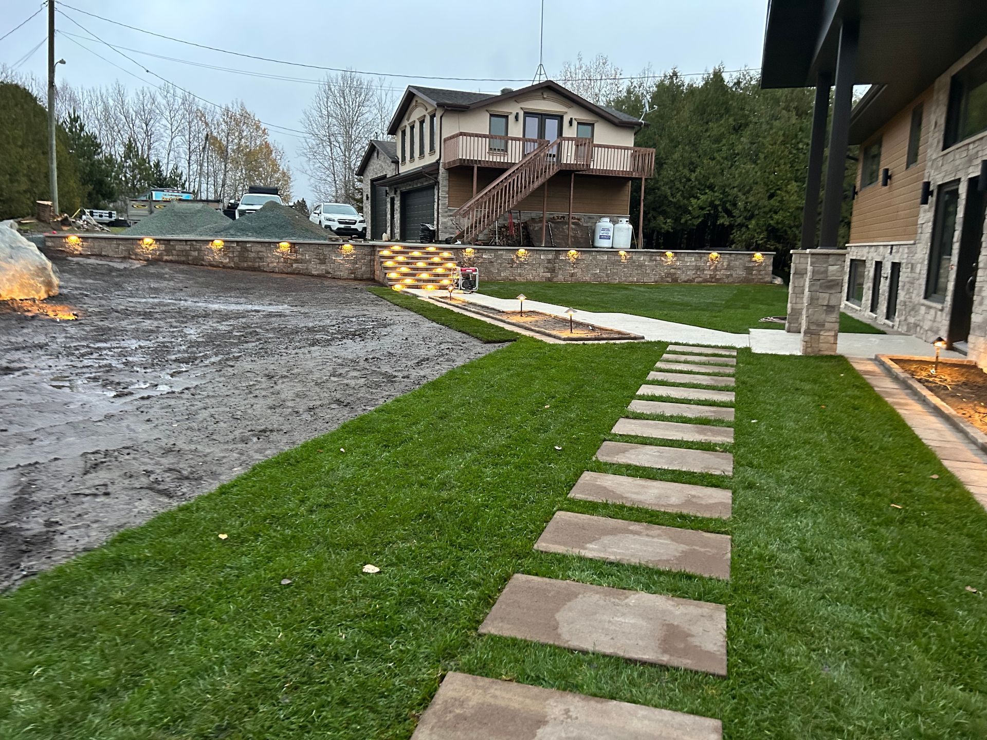Chemin de dalles traversant un chantier boueux, bordé de maisons et d'une pelouse verte.