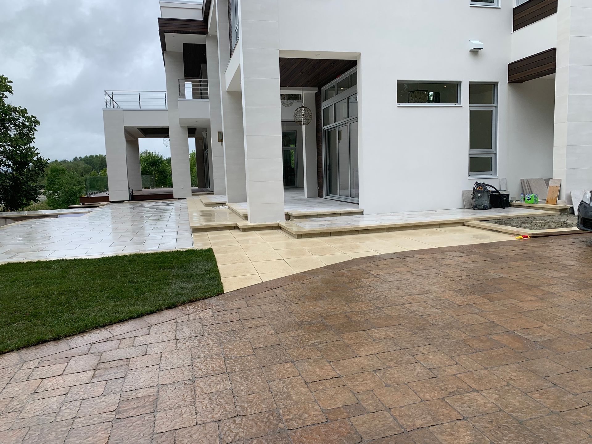 Maison moderne blanche avec allée en briques humides, terrasse et coin salon extérieur.