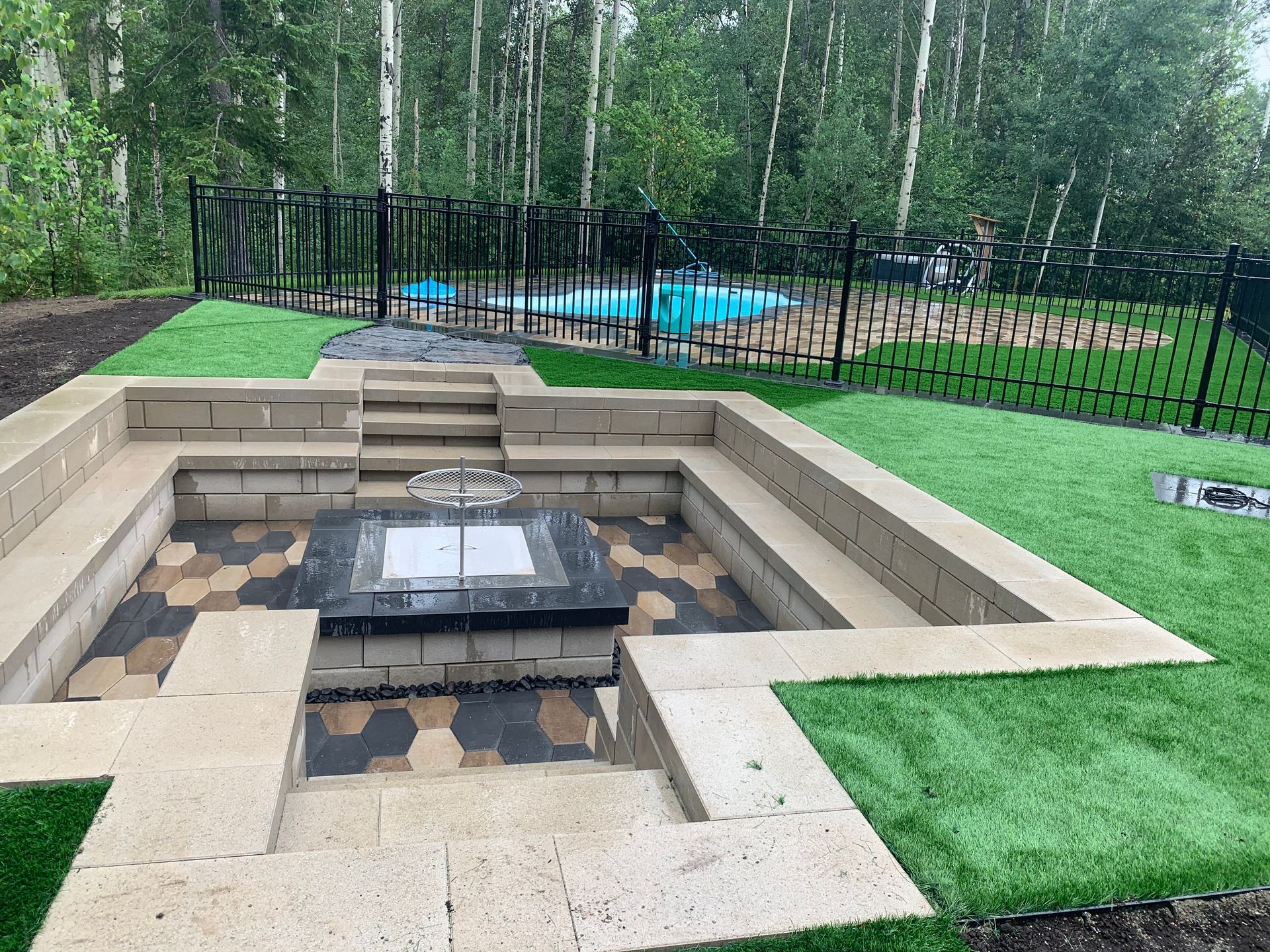 Foyer extérieur encastré dans la cour arrière avec sièges en pierre, gazon vert et piscine clôturée en arrière-plan