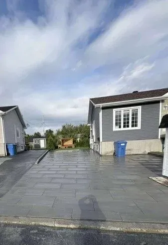 Allée pavée mouillée entre des maisons grises sous un ciel nuageux, avec des poubelles bleues près des entrées.