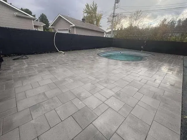 Cour arrière avec terrasse en pavés gris et petite piscine ronde enterrée, bordée d'une clôture noire