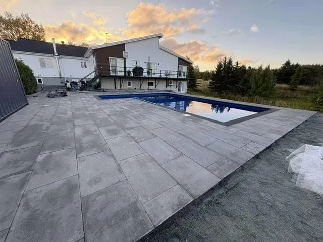 Terrasse arrière avec piscine rectangulaire au coucher du soleil, à côté d'une maison blanche et d'une cour en gravier