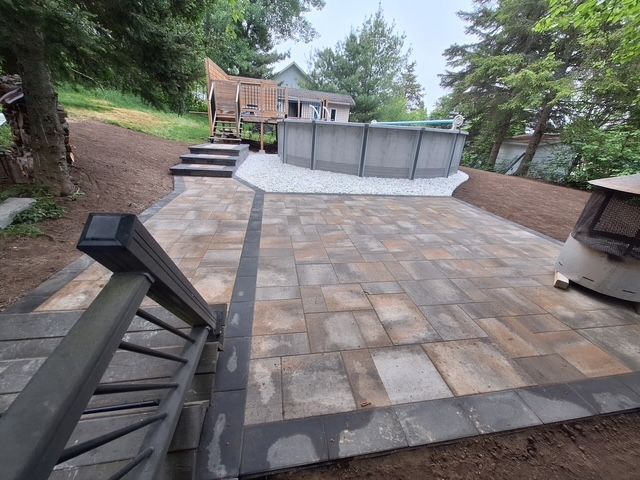 Terrasse en pierre avec foyer, marches et sièges extérieurs dans une cour arrière boisée