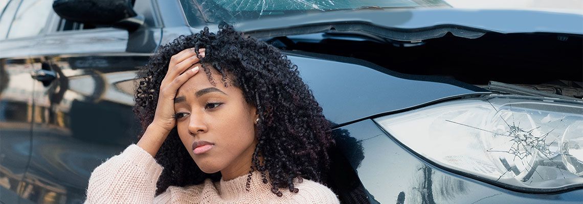 A woman is standing in front of a damaged car.