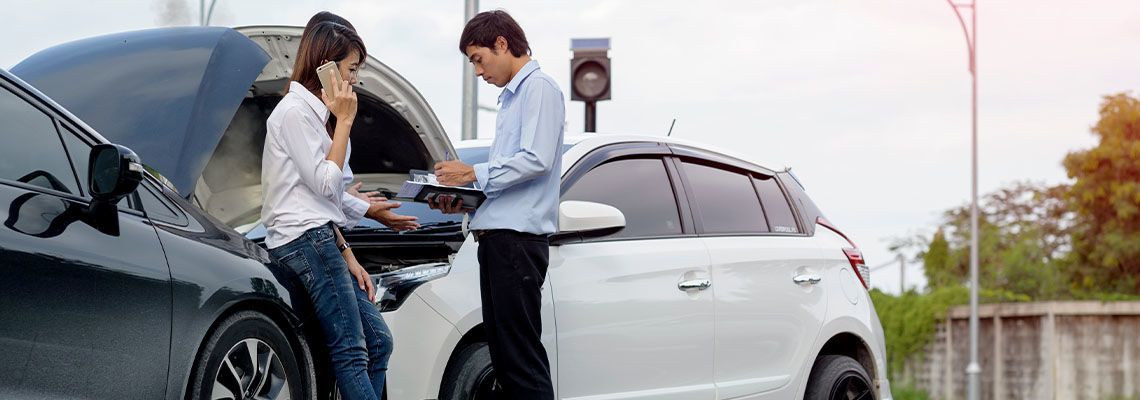 A man and a woman are standing next to a broken down car.