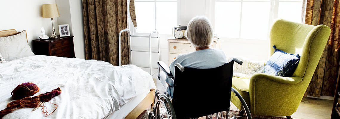 An elderly woman in a wheelchair is sitting in a bedroom next to a chair. An elderly woman in a wheelchair is sitting in a bedroom next to a chair.