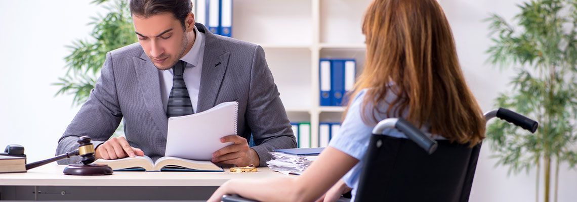 A woman in a wheelchair is sitting at a desk with a lawyer.