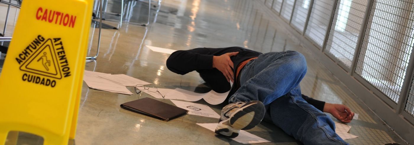 A man is laying on the floor next to a yellow caution sign. A man is laying on the floor next to a yellow caution sign.
