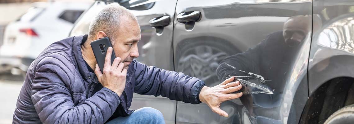 A man is talking on a cell phone next to a damaged car. A man is talking on a cell phone next to a damaged car.