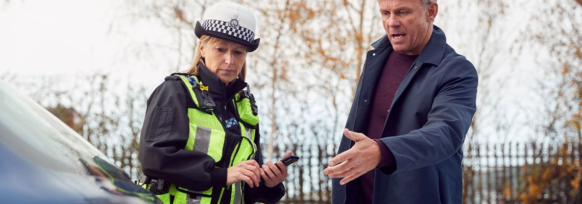 A police officer is talking to a man in front of a car.
