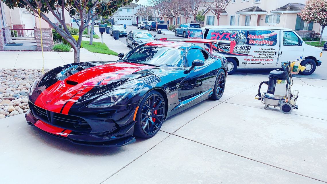 A black and red sports car is parked in a driveway next to a van.