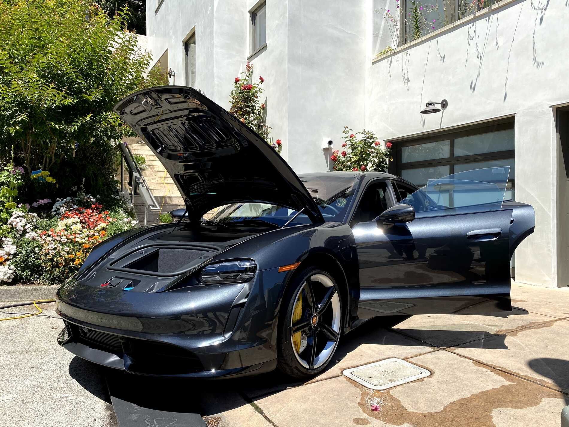 A black sports car with the hood up is parked in front of a garage.