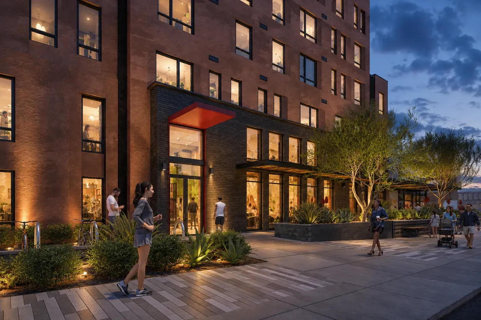 Modern apartment building entrance and exterior at dusk with people walking by.