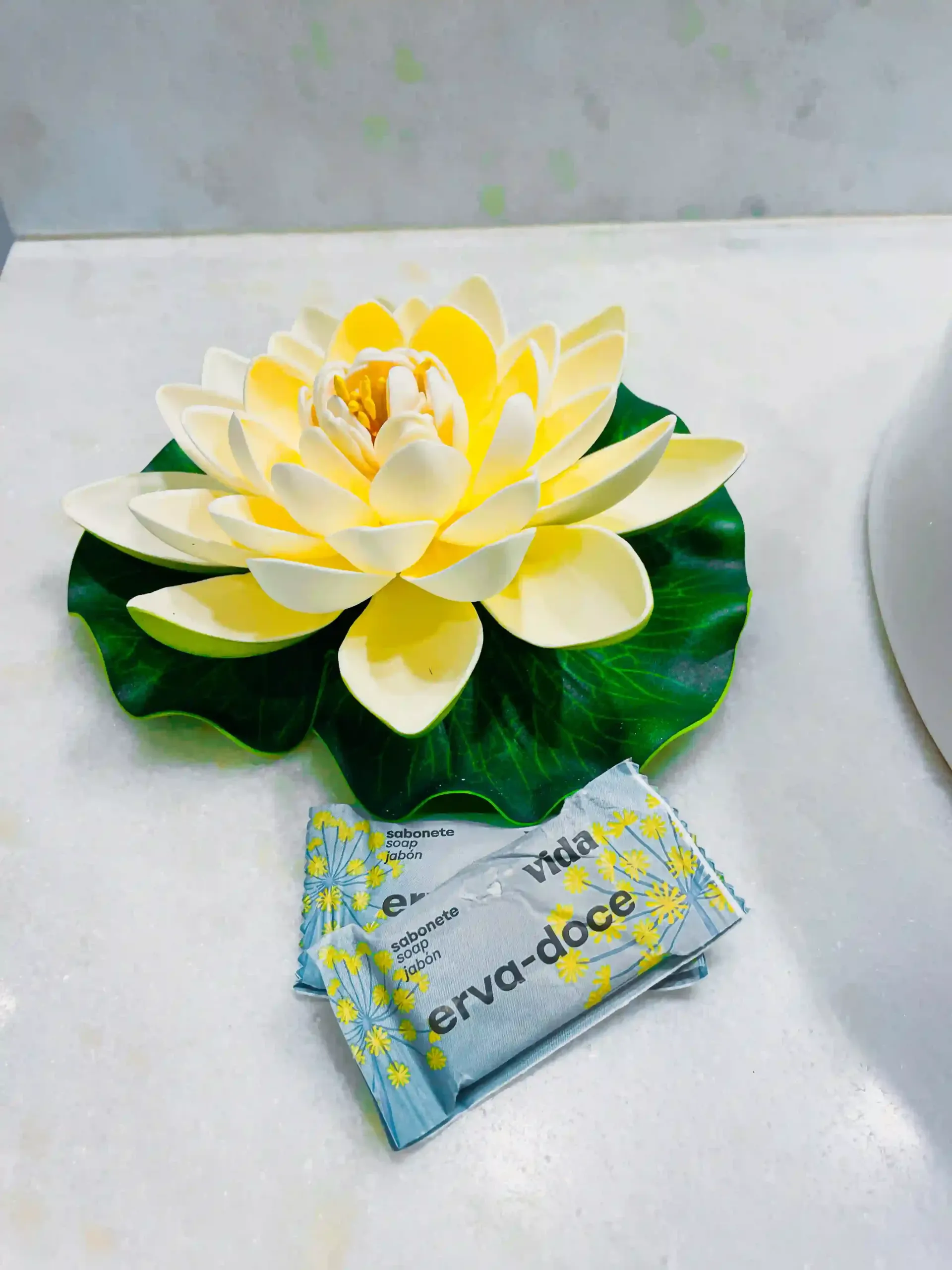 Arranjo de flores amarelo-e-branco sobre uma base de folhas verdes com um pequeno cartão estampado sobre uma superfície branca.