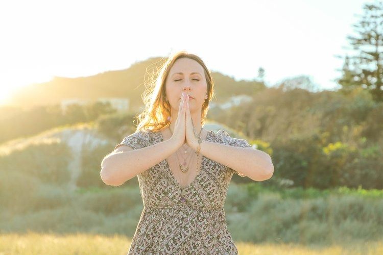 A Woman Is Standing In A Field With Her Hands Folded In Prayer — The Enchanted Wolf Holistic Port Macquarie, NSW