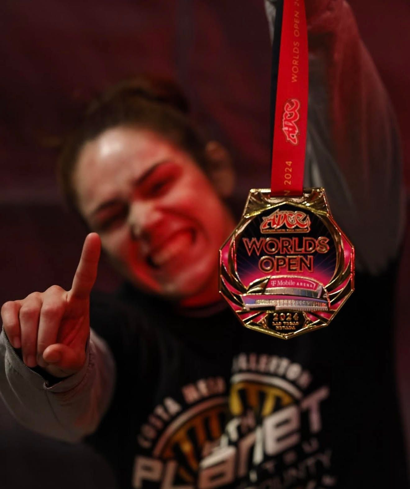 Person posing with raised finger beside a red medal labeled “World Open” against a red background