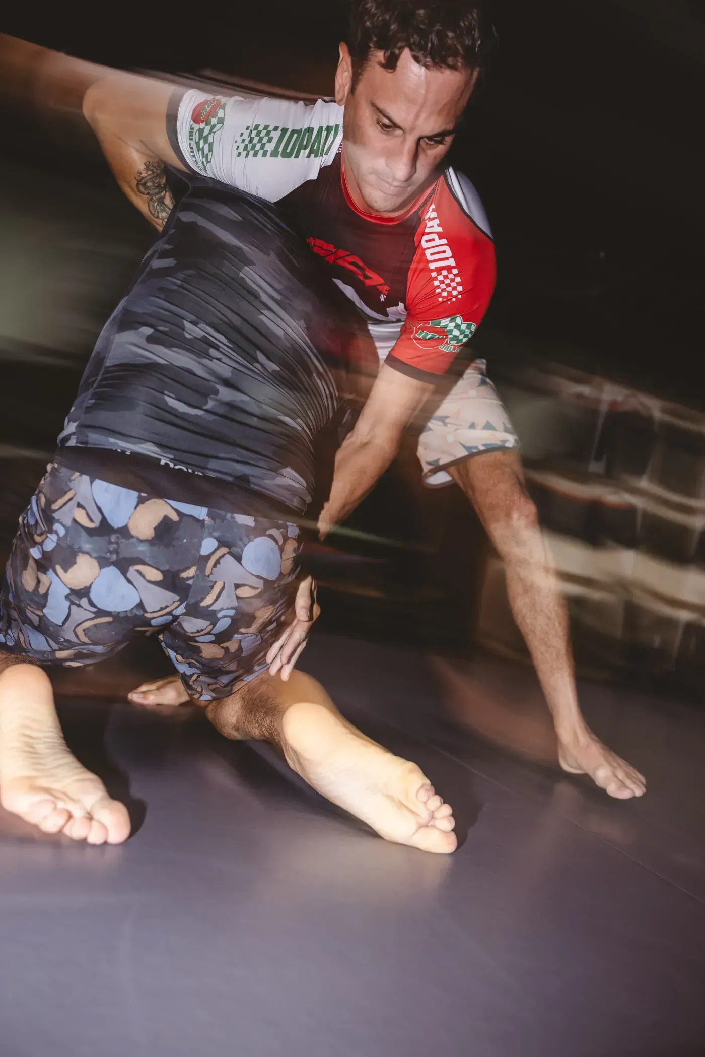 Two wrestlers grappling on a mat, one in red and black, blurred motion in action