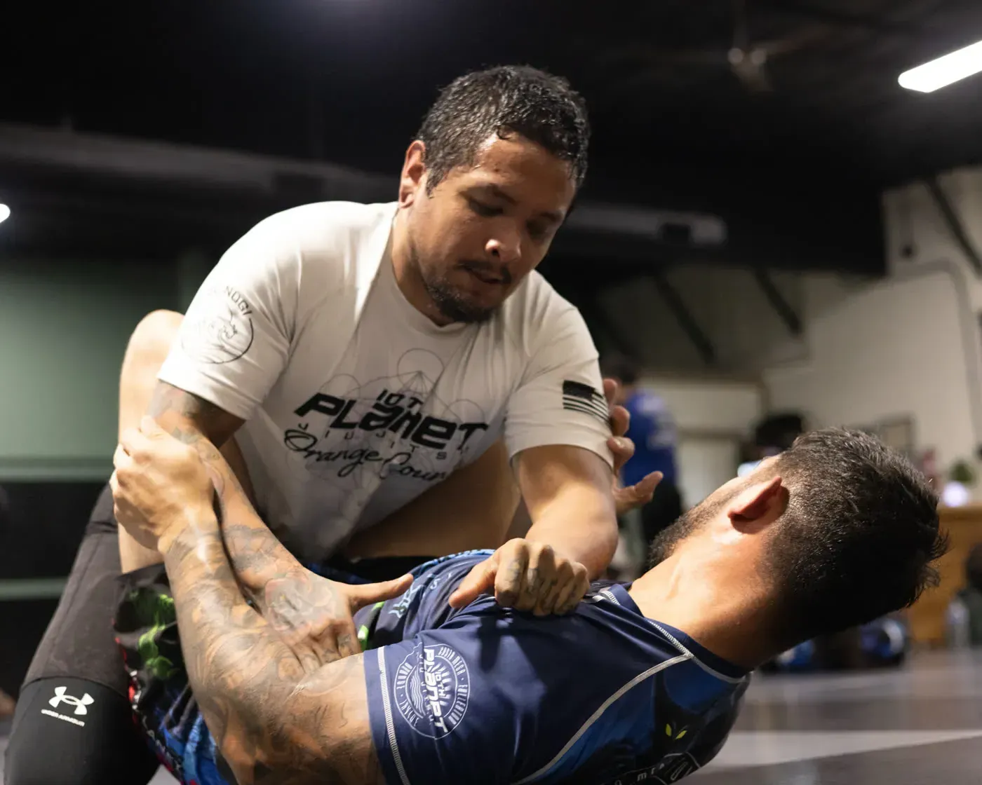 Two men grappling in a gym, one leaning over the other during a training drill.