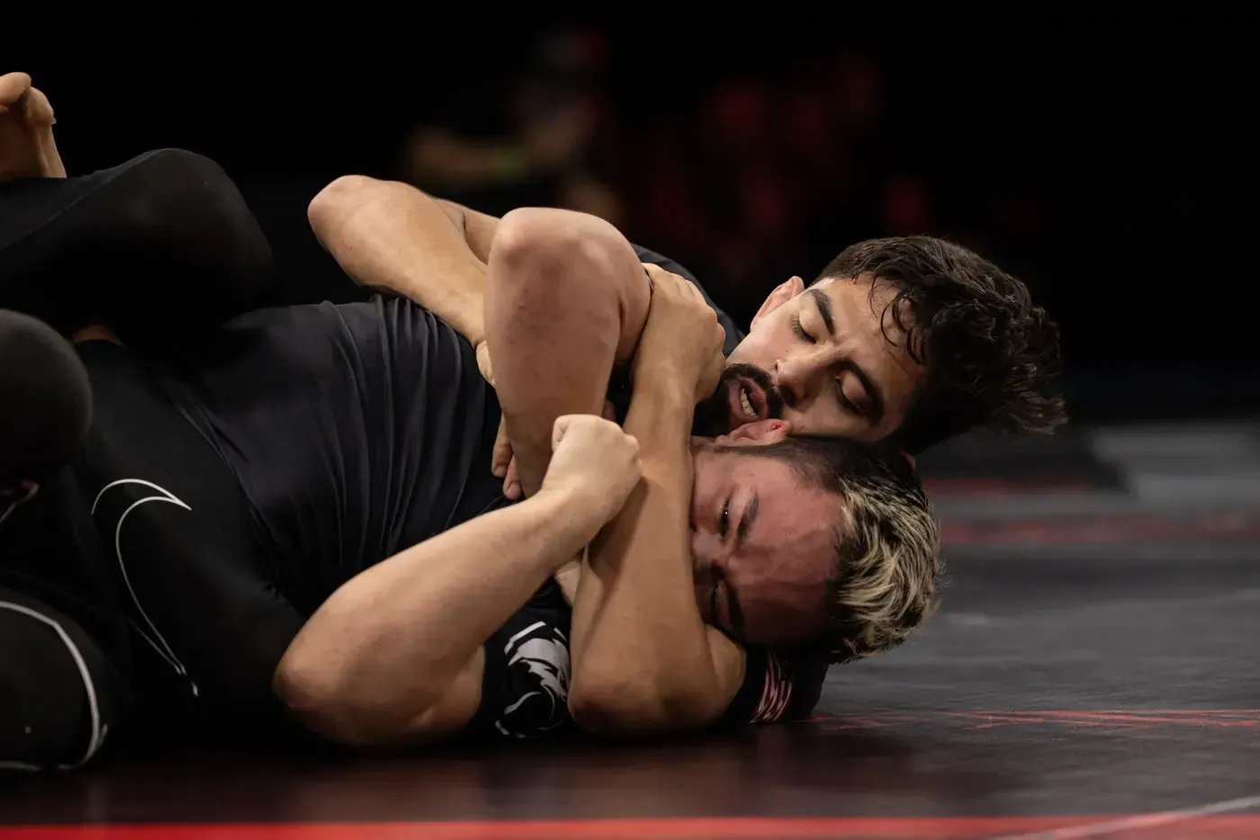 Two wrestlers grapple on a mat, one pinning the other in a tight hold.