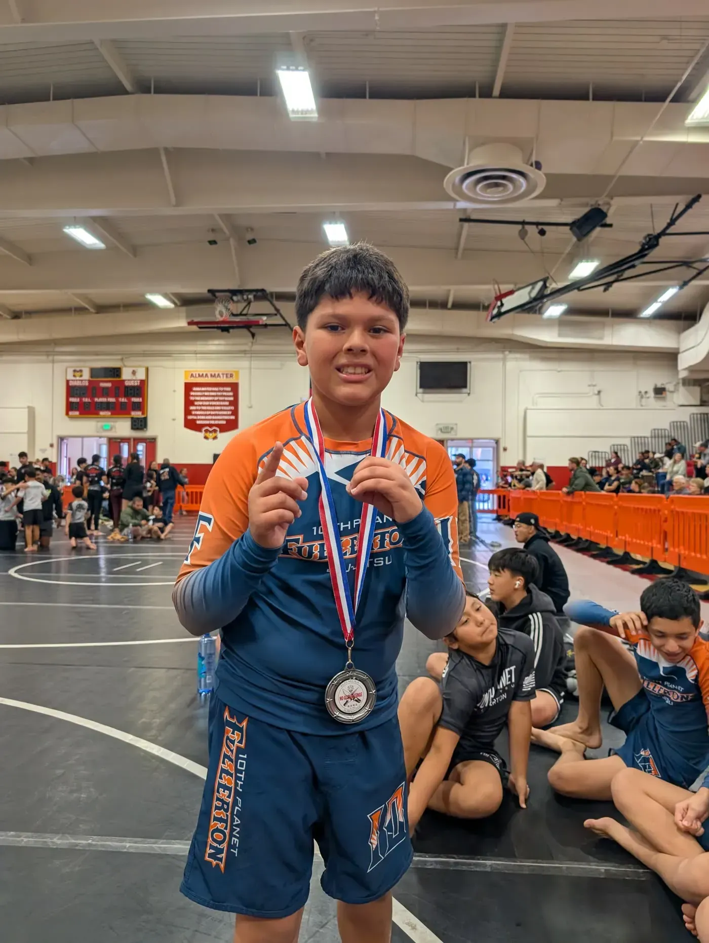 Young wrestler in blue singlet holding a silver medal in a gymnasium after a match