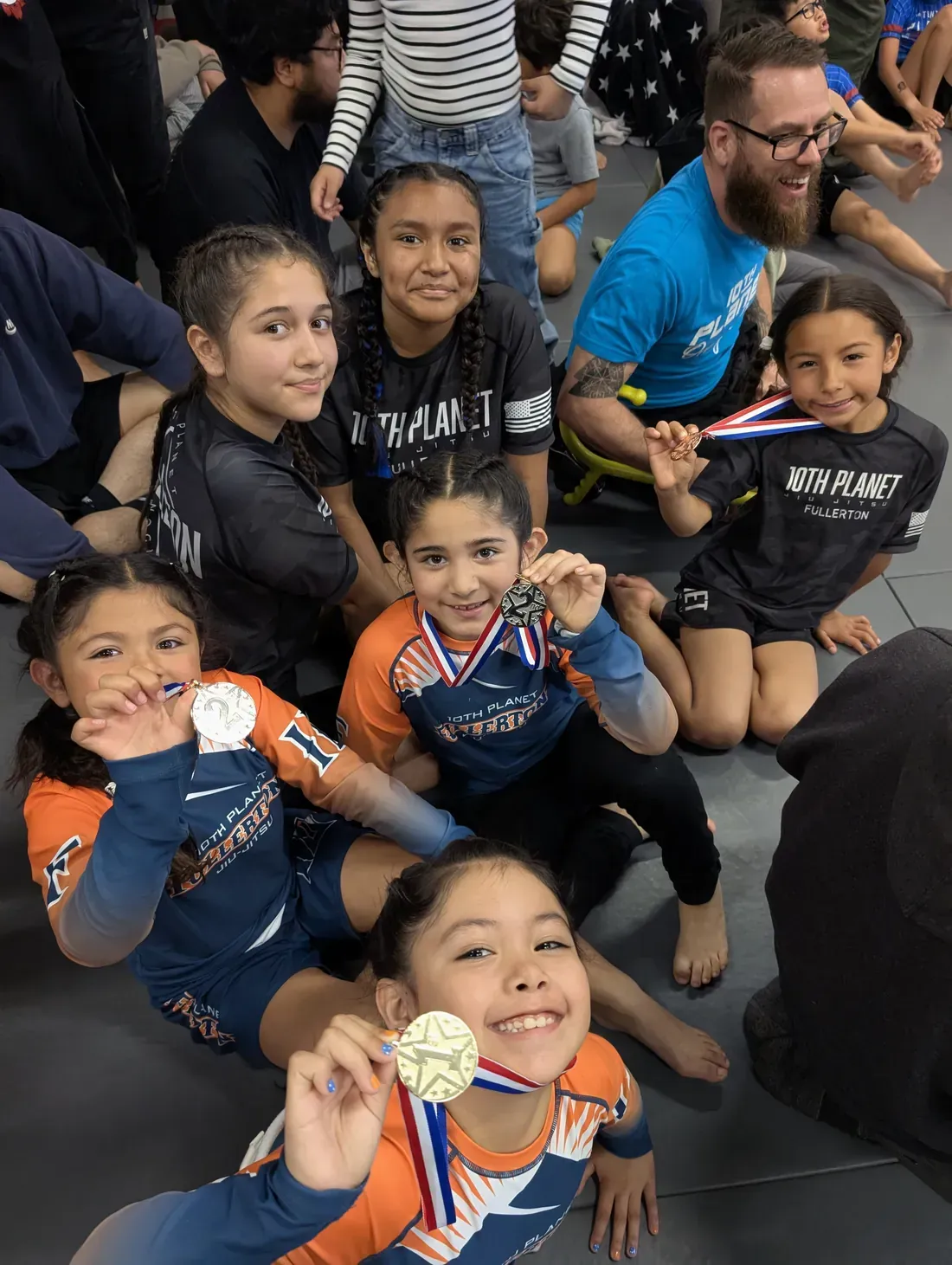 Children posing with medals in a crowded indoor event setting.