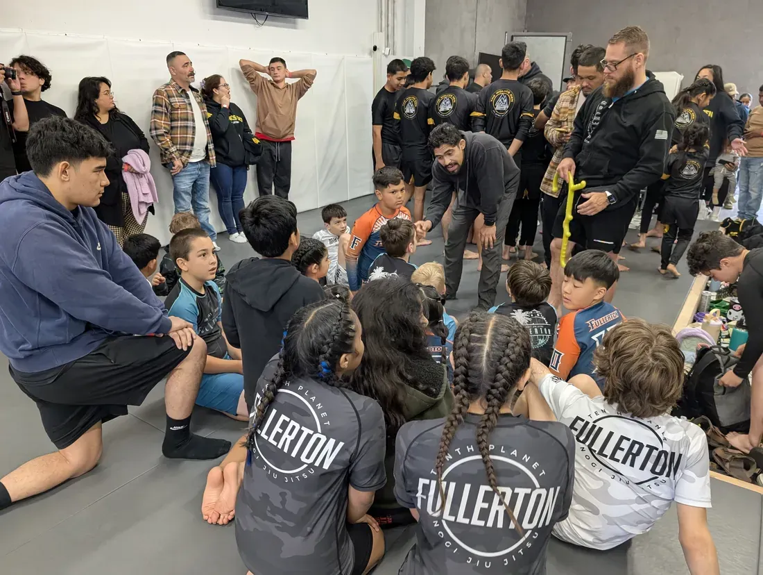 Children seated on the floor listening to adults in a gym or dojo during a group activity