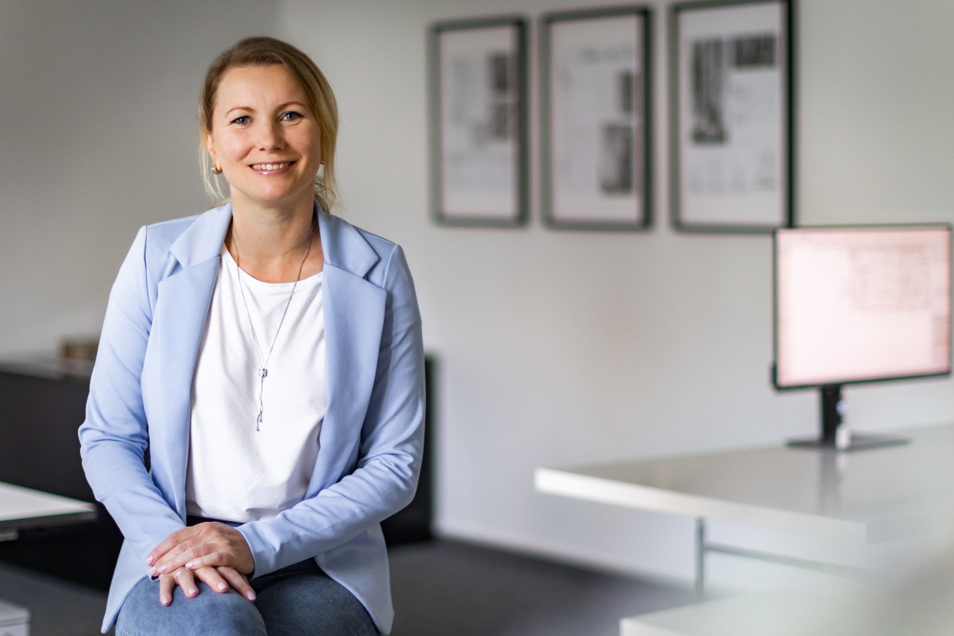 Eine Frau in einer blauen Jacke sitzt an einem Schreibtisch vor einem Computer.