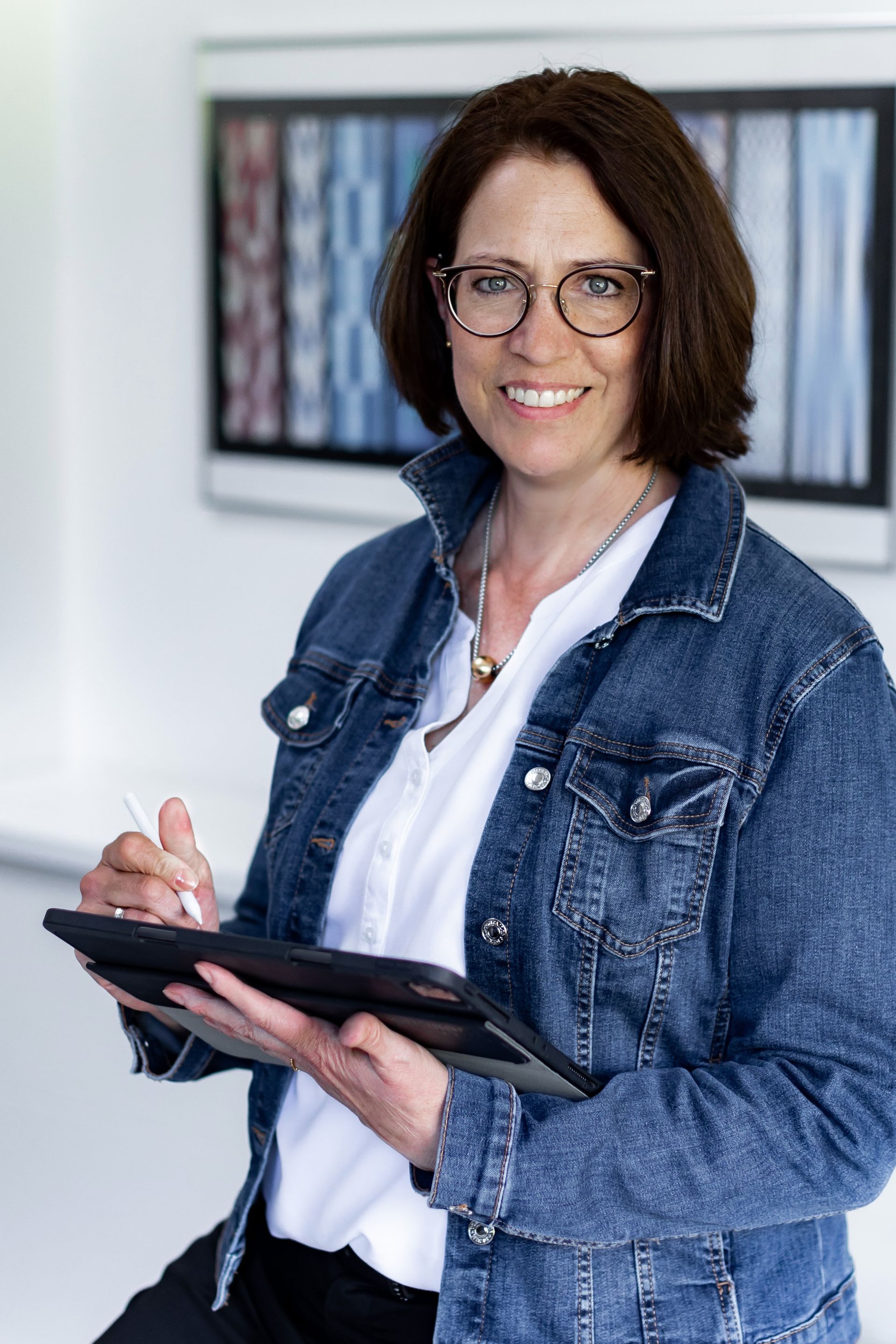 Eine Frau in einer Jeansjacke hält ein Tablet und lächelt