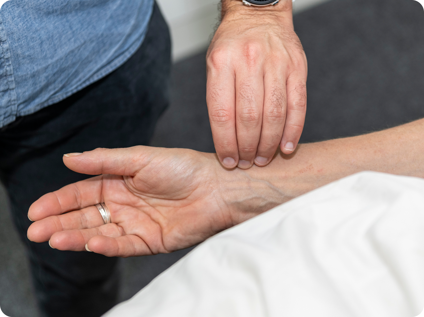 A person's wrist being checked for pulse by another person's fingers.