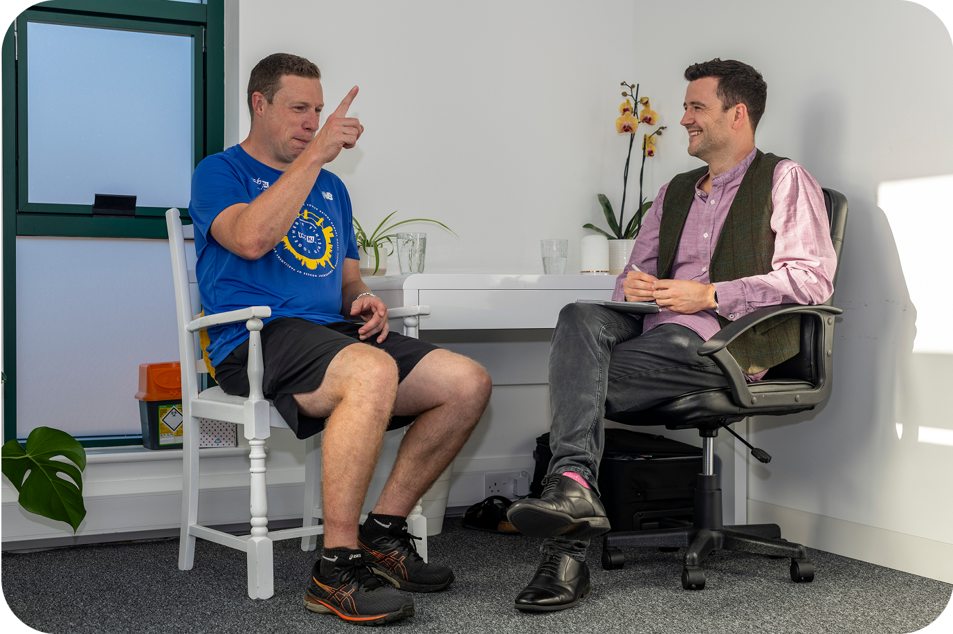 An acupuncture consultation where a male patient is sitting to the left of the acupuncturist whilst explaining his health.