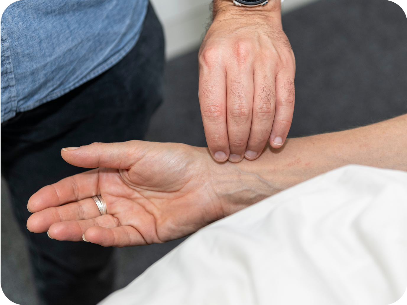 A close-up of an acupuncturist reading a patient's pulse who is lying down. It's a key diagnostic pillars of acupuncture.