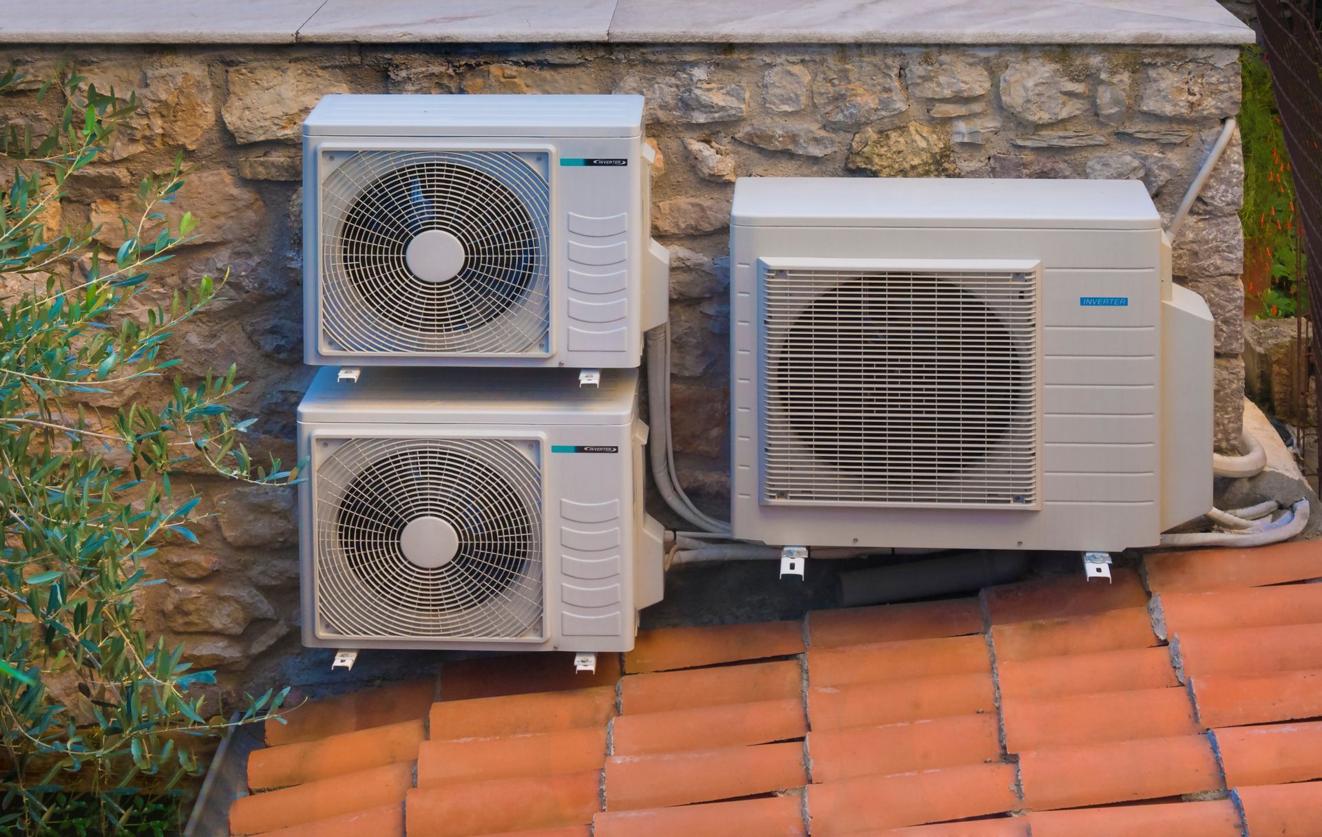 Two air conditioners are stacked on top of each other on a tiled roof.
