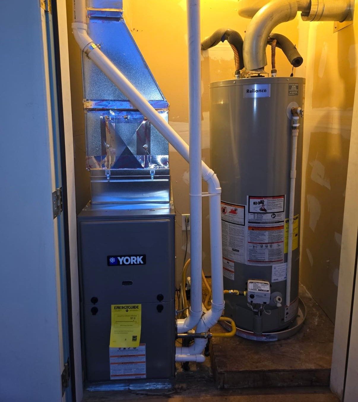 A York furnace and a water heater installed inside a utility closet, with connected white PVC pipes and metal ductwork.