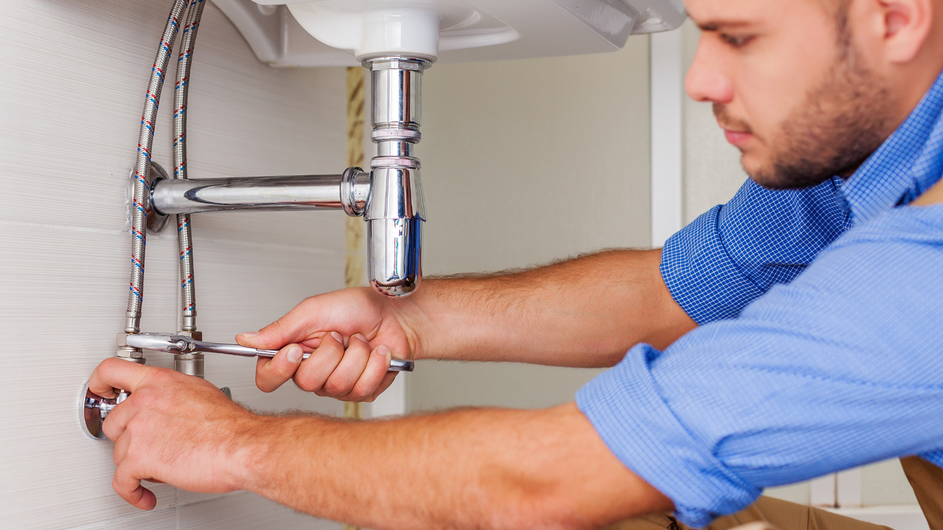 Plumber tightening pipes under a sink with a wrench