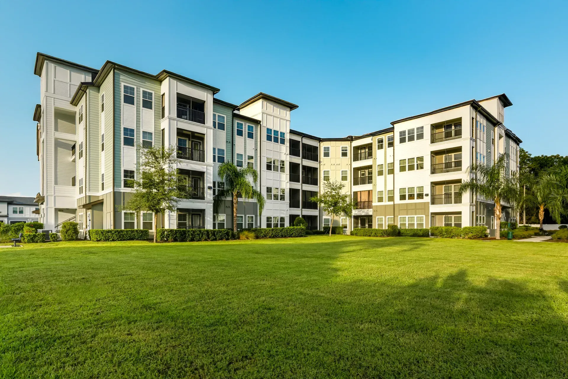 Modern apartment buildings with white and beige facades beside a large green lawn