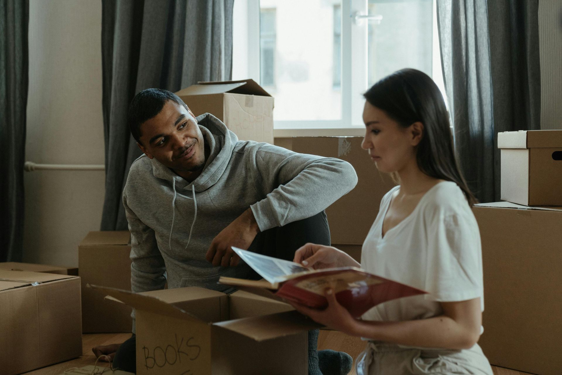 Two people reviewing paperwork among moving boxes in a sunlit room
