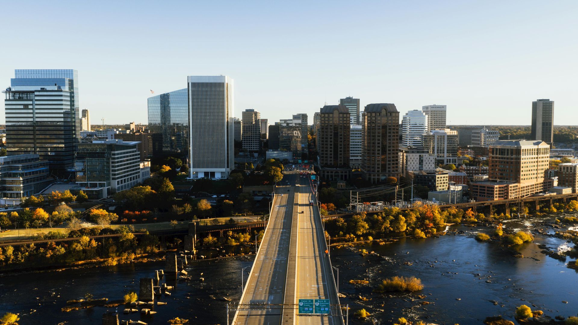 City skyline at dusk with a lit bridge spanning a river, framed by modern high-rise buildings.