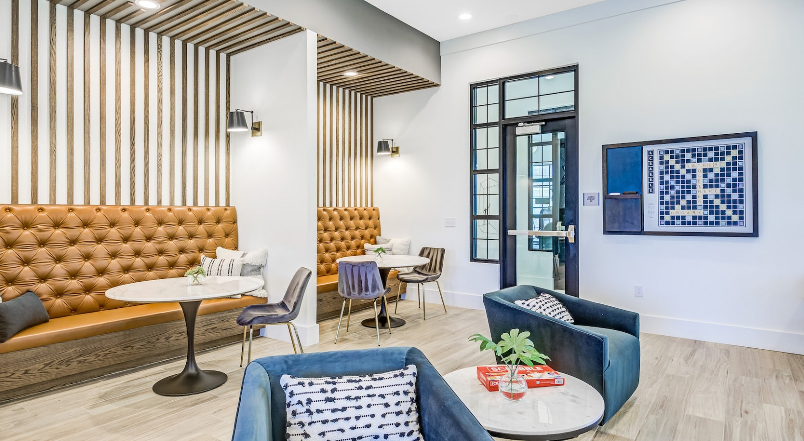 Modern lounge with tufted tan bench seating, blue chairs, white walls, and light wood floors