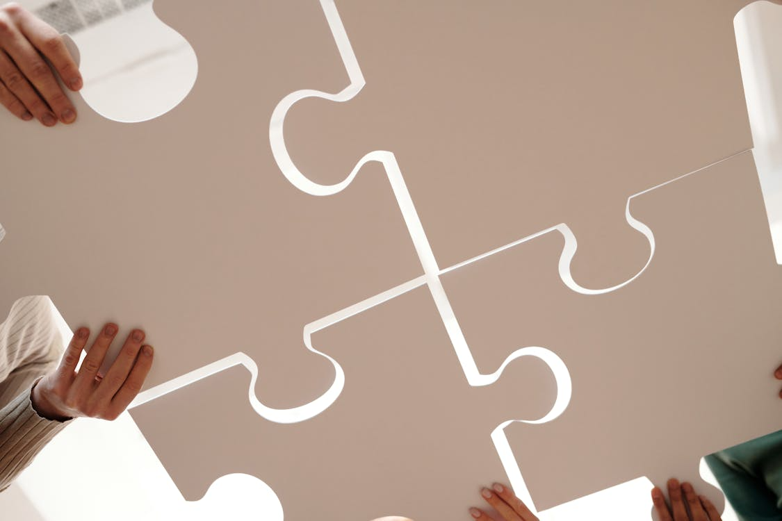 Hands assembling white puzzle pieces on a beige surface