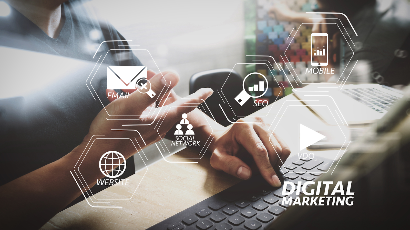 Two people working at a desk with digital marketing icons overlaid on a blurred office background.