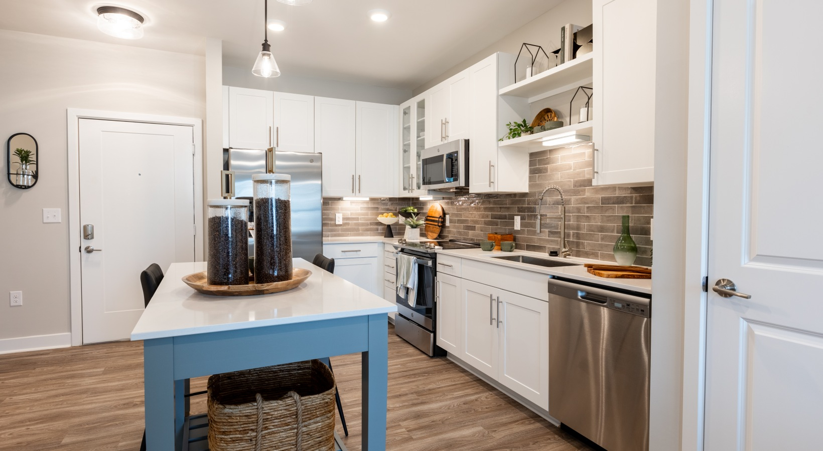 Bright modern kitchen with white cabinets, stainless appliances, and a blue island table.