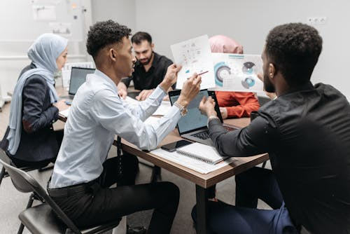 Team collaborating around a laptop and sketches in a bright office meeting room.