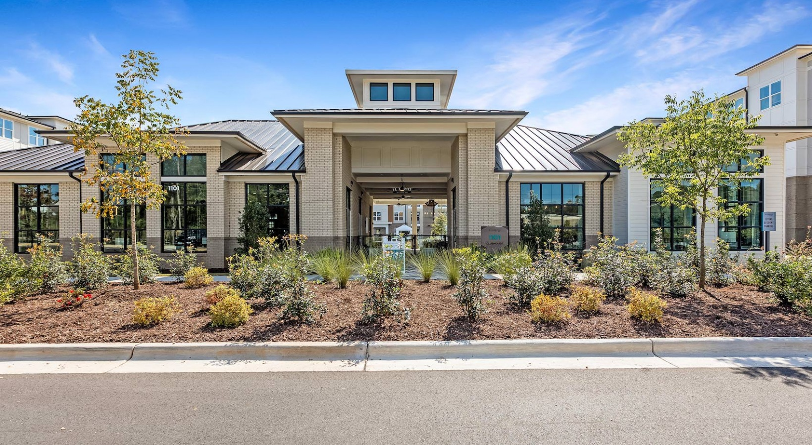 Modern single-story building with large windows, landscaped shrubs, and a central entrance under a blue sky