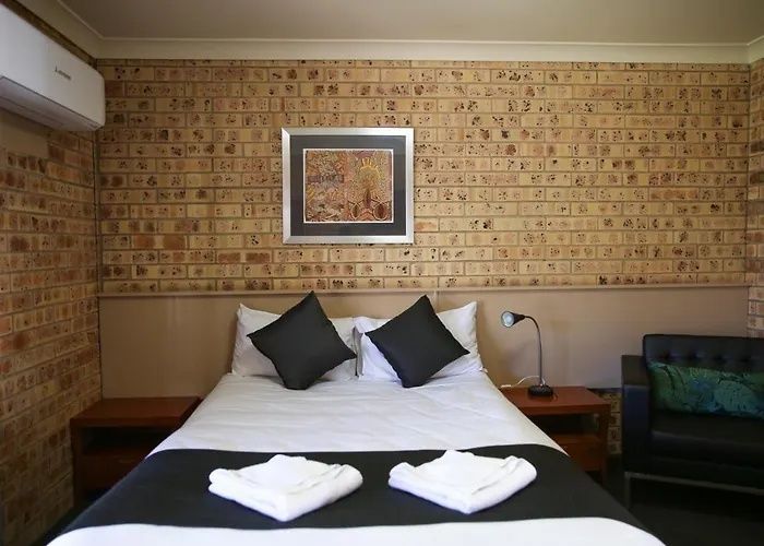 Bedroom with a bed, black pillows, folded towels, and a framed wall picture above the headboard