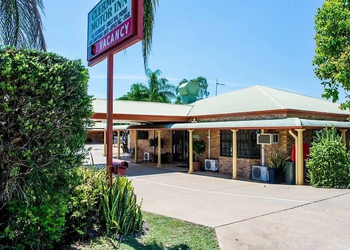 Small roadside motel with a red sign, white roof, and palm trees in bright sunlight