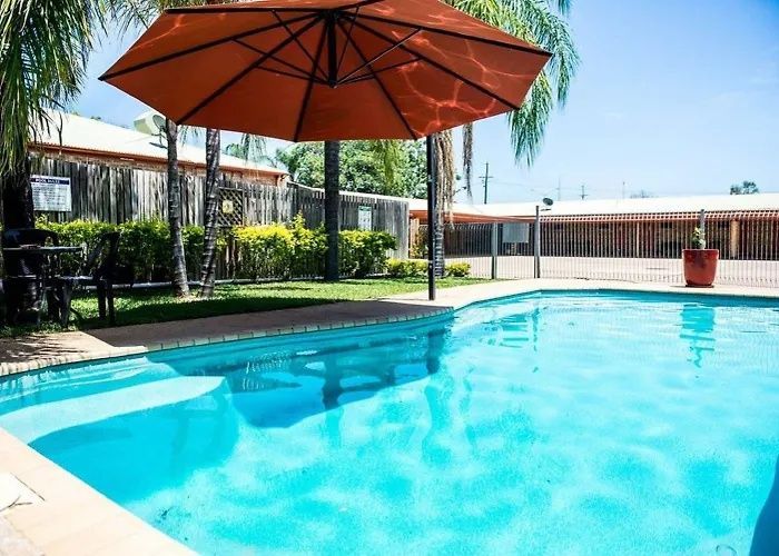 Swimming pool with turquoise water, orange umbrella, and lounge area in a sunny outdoor courtyard