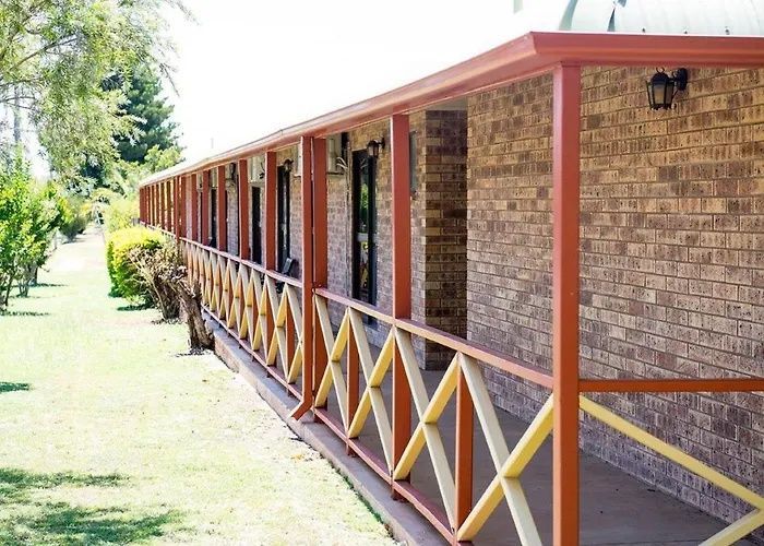 Long brick corridor with red posts and yellow cross-braced railings beside a grassy path.