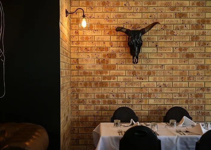 Cozy restaurant table with white linens against a brick wall, decorated with a mounted bull skull and warm wall lamp.