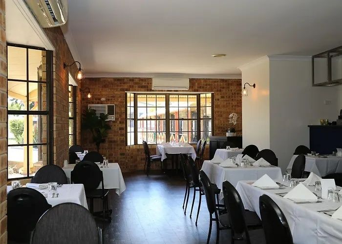 Elegant restaurant dining room with set tables, black chairs, brick walls, and sunlight from large windows